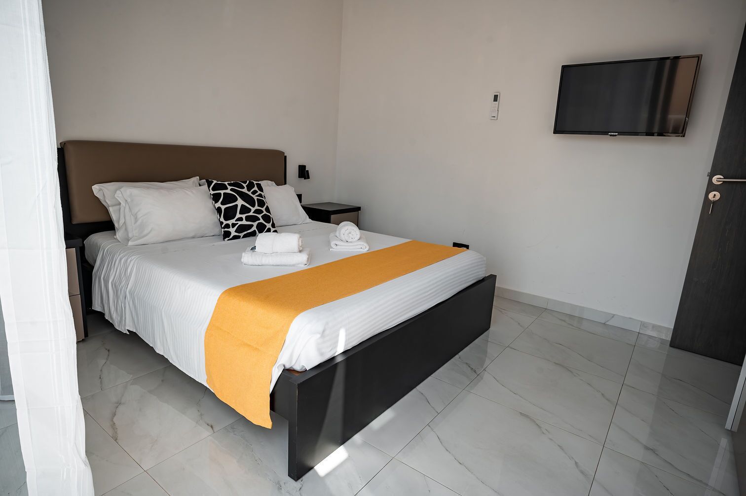 A modern hotel room with a bed, a nightstand, a TV, and a door.
