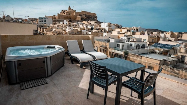 Een terras op het dak met een jacuzzi, lounge fauteuils en een tafel met uitzicht op een historische stad.