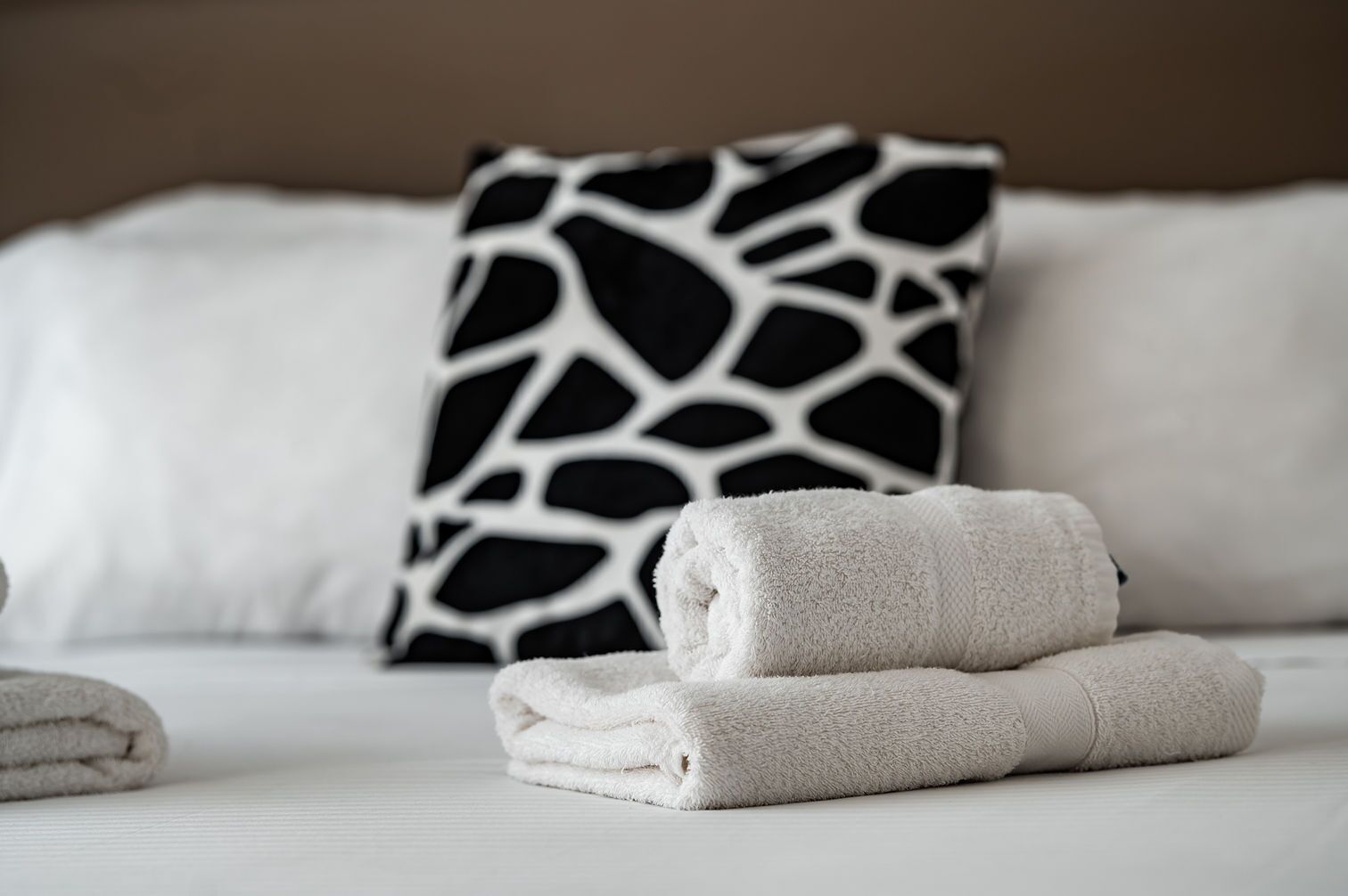 Una cama bien hecha con sábanas blancas y un cojín estampado en blanco y negro.