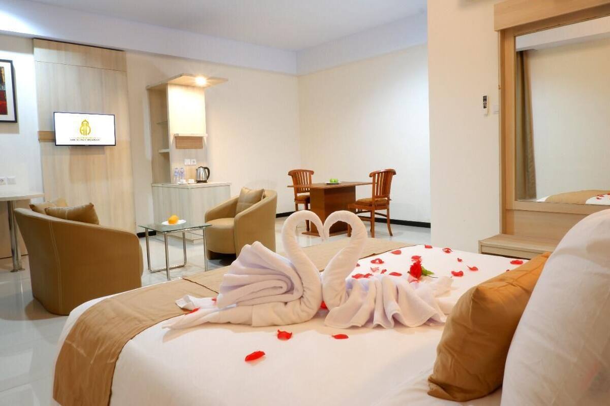 A hotel room with a bed, two chairs, a small table, a TV, and a mirror.