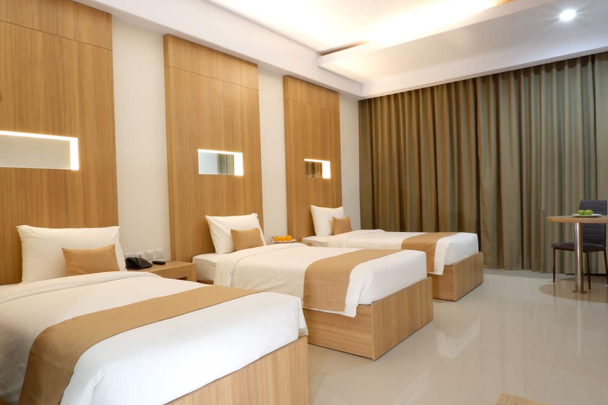 A hotel room with three beds, wooden headboards, and a small table with a chair.