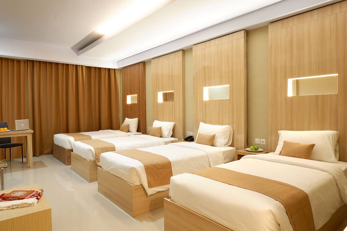 A hotel room with four beds, a desk with a laptop, and a small table with fruit.