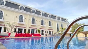 A swimming pool with a tiled deck and a metal railing. In the background, there is a large building with multiple windows and balconies. - Sahid Azizah Syariah Hotel & Convention (Kendari)