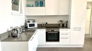 Una cucina moderna con mobili bianchi, un lavello in acciaio inossidabile, un forno a microonde, una macchina da caffè e un forno integrato.
