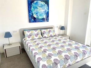 A neatly made bed with a patterned bedspread, two bedside lamps, a nightstand, and a wall painting. - Small lake view paradise with private pool (Riva di Solto)