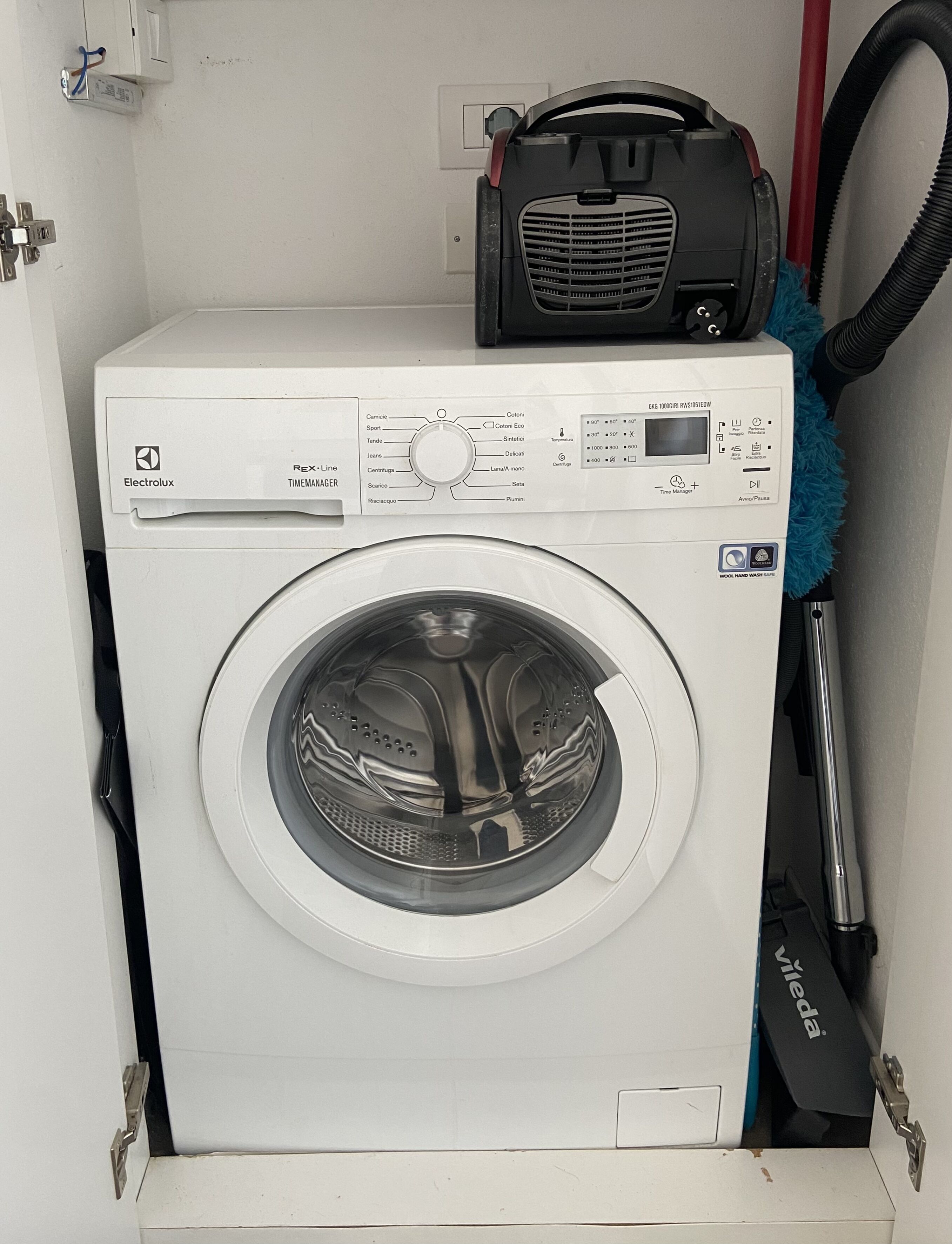 A white Electrolux Rex-Line Timemanager washing machine with a control panel, a vacuum cleaner, and a blue cleaning brush.