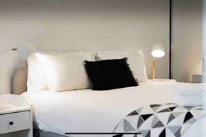 Cozy retreat with a neatly made bed, bedside table, and wall-mounted mirror.