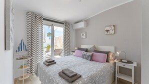 Une chambre à coucher comprenant un lit, des tables de chevet, une commode, une fenêtre avec des rideaux, un ventilateur de plafond et une vue sur l’extérieur.