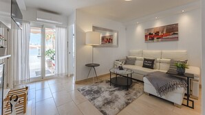 Un salon moderne avec un canapé, une table basse et un grand miroir. Une porte donne sur un balcon agrémenté de plantes.