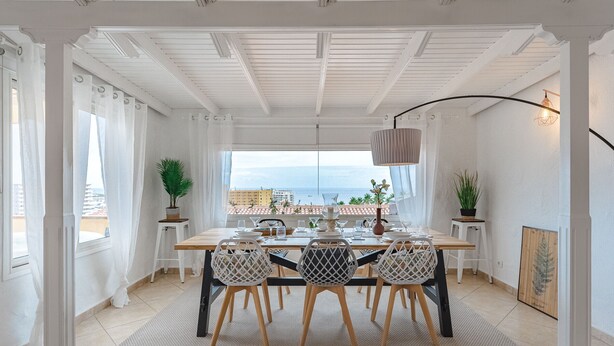 A dining area with a table set for four, white chairs, a hanging light fixture, and a view of the sea. - Ferienwohnung Penthouse Eden - Costa Adeje (Adeje)