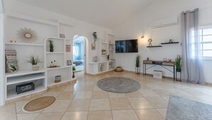 A spacious living room with a flat-screen TV, white shelving, and a large window with curtains. - Ferienwohnung Penthouse Eden - Costa Adeje (Adeje)