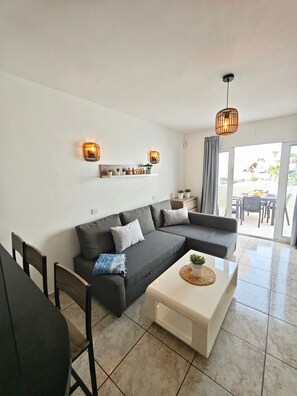 A modern living room with a grey sectional sofa, a white coffee table, and a dining area with a table and chairs. - Apartment Sea View  Holiday Valley -  Costa Adeje (Adeje)