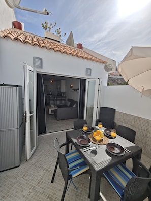 An outdoor dining area with a table set for two, chairs, and a view into the house. - Apartment Sea View  Holiday Valley -  Costa Adeje (Adeje)