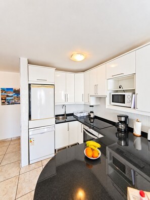 A modern kitchen with white cabinets, a black countertop, a refrigerator, a microwave, and a coffee maker. - Apartment Sea View  Holiday Valley -  Costa Adeje (Adeje)