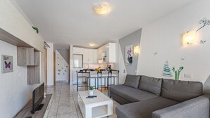 Una sala de estar moderna con un sofá gris, una mesa de centro blanca y una cocina al fondo.
