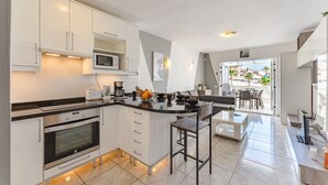 Una cocina moderna con armarios blancos, un microondas y un horno. Hay un comedor con una mesa y sillas, y vistas al exterior.
