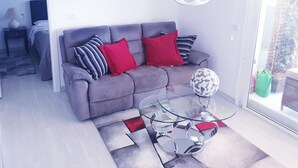 En moderne stue med en grå sofa, røde og stribede puder, et glasbord og et stort, abstrakt lysarmatur.