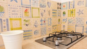Eine Küche mit einem Gasherd und einem weißen Eimer. Die Wand ist mit bunten Fliesen verziert.