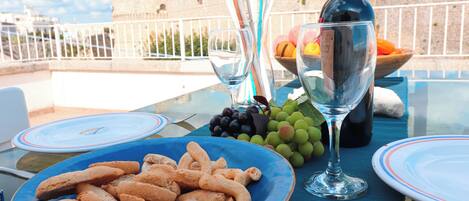 A table set with a plate of snacks, a bottle of wine, and glasses, with a scenic view of a historic building in the background.