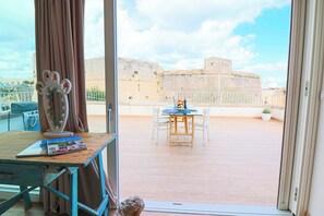 A balcony with a table and chairs, a view of a historic building, and a potted plant.