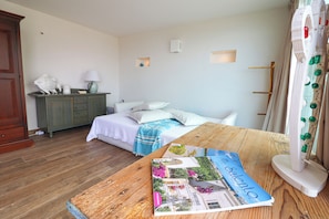A bedroom with a bed, a wooden table with a magazine, a dresser, and a mirror.
