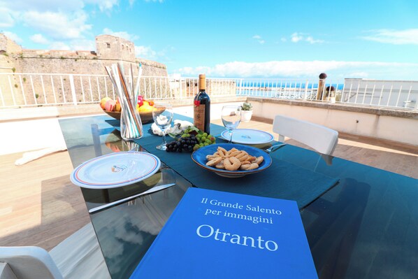 A table set for a meal with a view of the sea and a historic building in the background. - Casa Sveva Romantic Studio With Panoramic Terrace in the Heart of Otranto (Otranto)