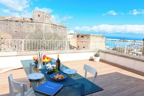 A table set for dining with a view of a historic stone wall and the sea. - Casa Sveva Romantic Studio With Panoramic Terrace in the Heart of Otranto (Otranto)