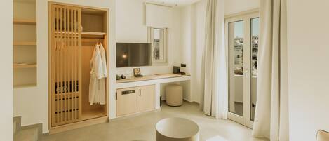 A modern hotel room with a wooden wardrobe, a vanity with a mirror, a flat-screen TV, a round seating area, and a balcony with curtains.