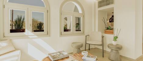 A well-lit room with a wooden coffee table, a white sofa, and two arched windows with plants.