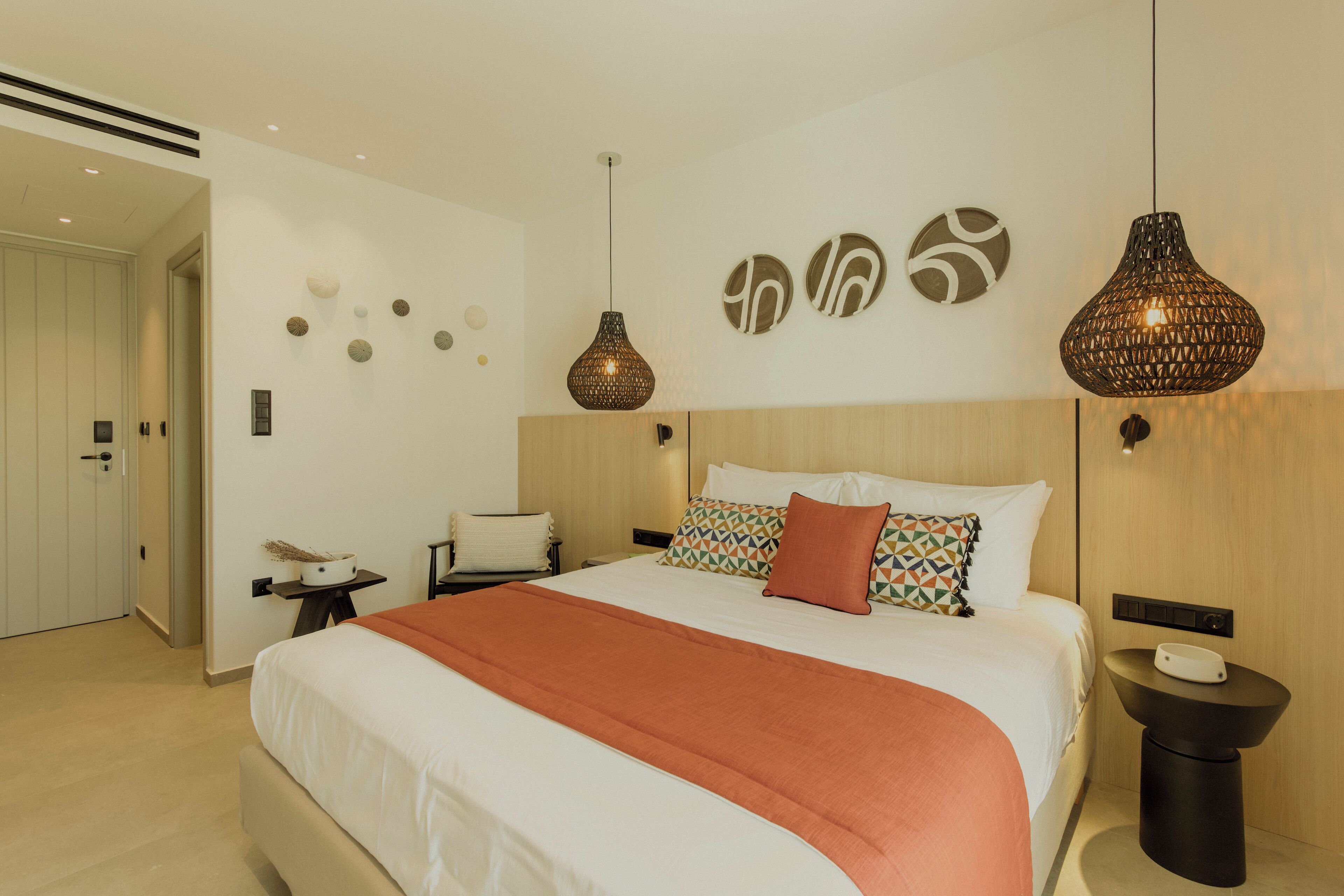 A modern hotel room with a large bed, two pendant lights, a bedside table, and a wall-mounted control panel.