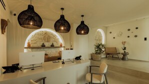 A modern reception area with a white desk, two wicker pendant lights, a stone arch, and a seating area with two chairs. - Opal Paros (Paros)