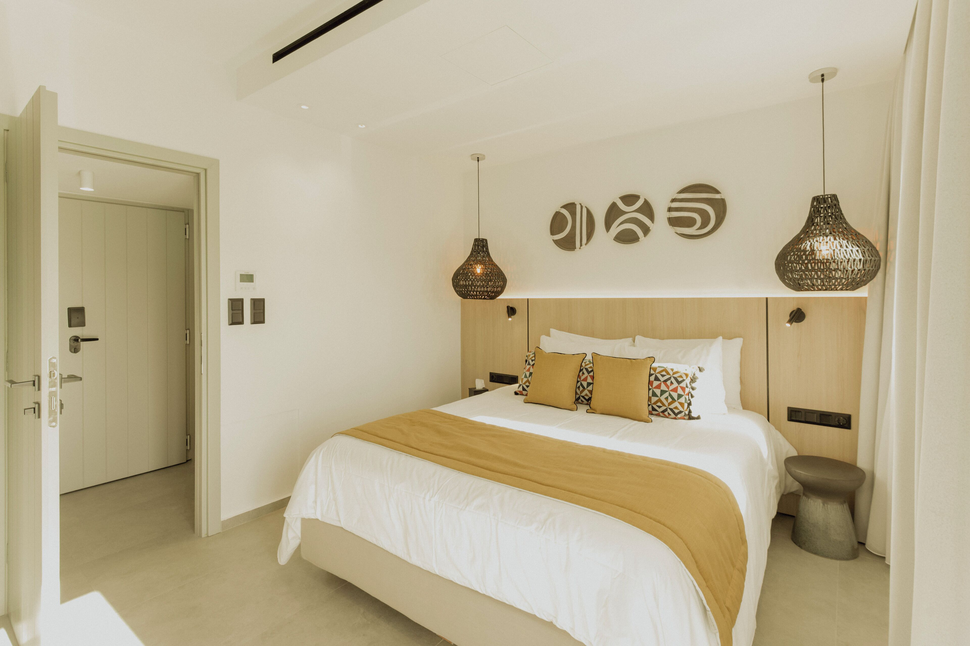 A modern hotel room with a large bed, a wooden headboard, and two pendant lights.