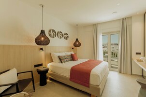 Een moderne hotelkamer met een groot bed, twee hanglampen, uitzicht op de stad en een balkon.