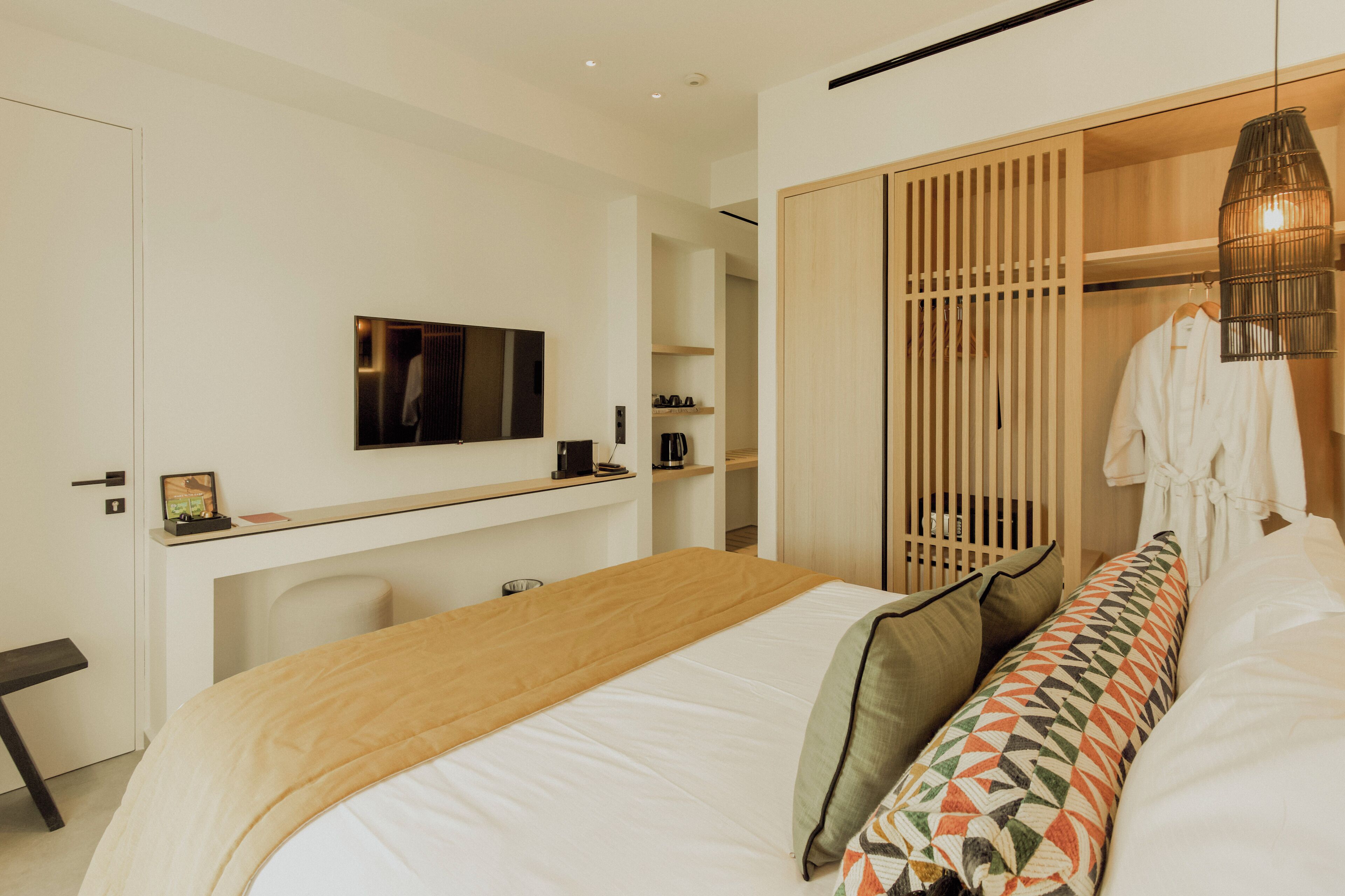 A modern hotel room with a bed, a desk with a TV, and a wardrobe.