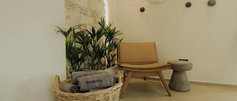 A room with a stone wall, a wicker basket with towels, a chair, and a small stool.