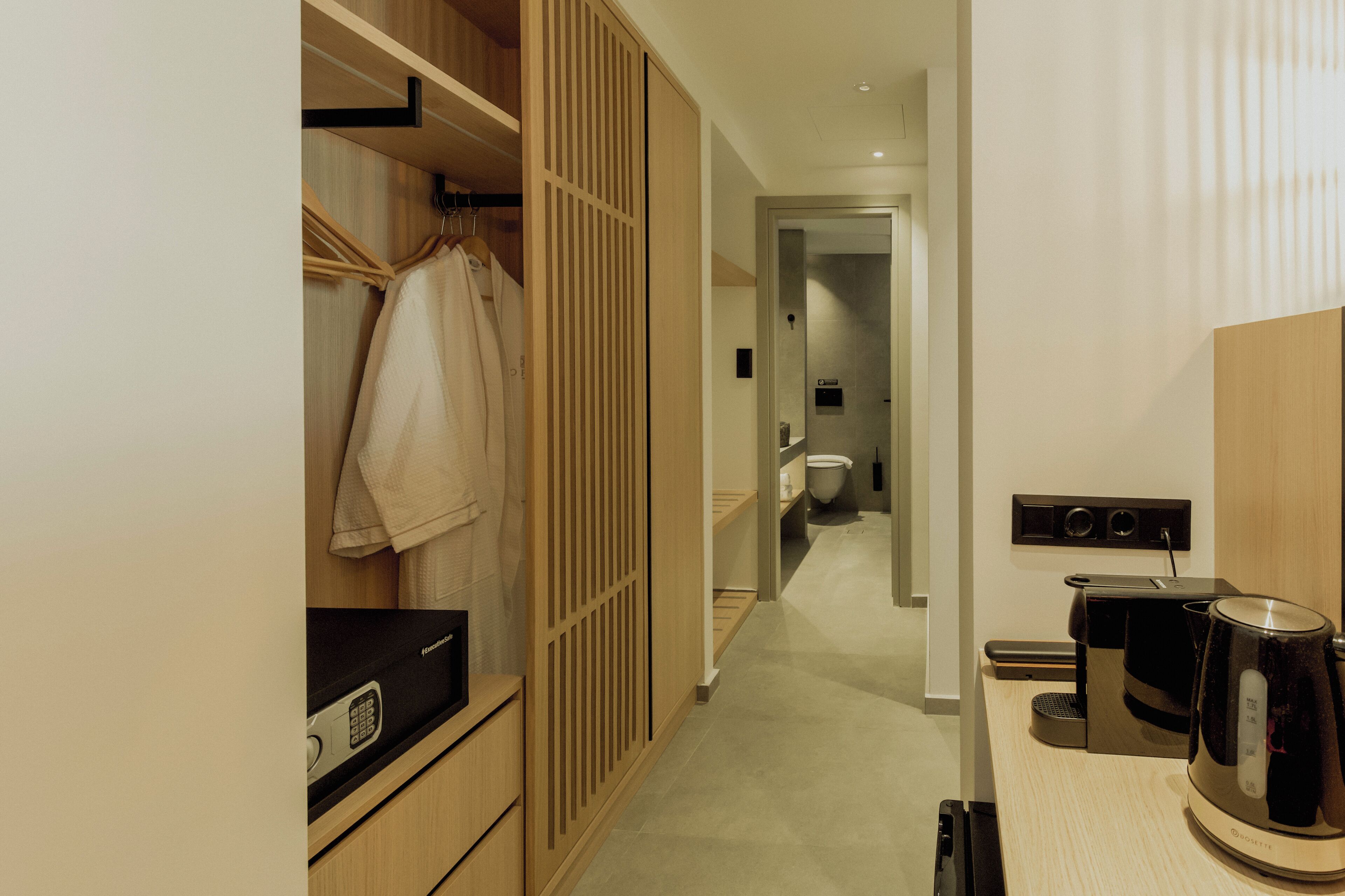 A hotel room with a wooden wardrobe, a small kitchenette with a coffee maker, and a toilet visible in the background.