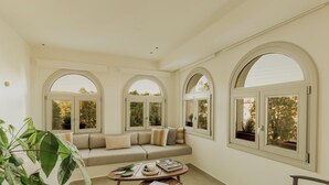 A spacious living room with a beige sofa, a coffee table, and large arched windows. - Opal Paros (Paros)