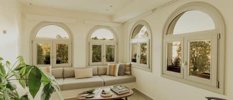 Amplia sala de estar con un sofá color beige, una mesa de centro y ventanas arqueadas grandes.