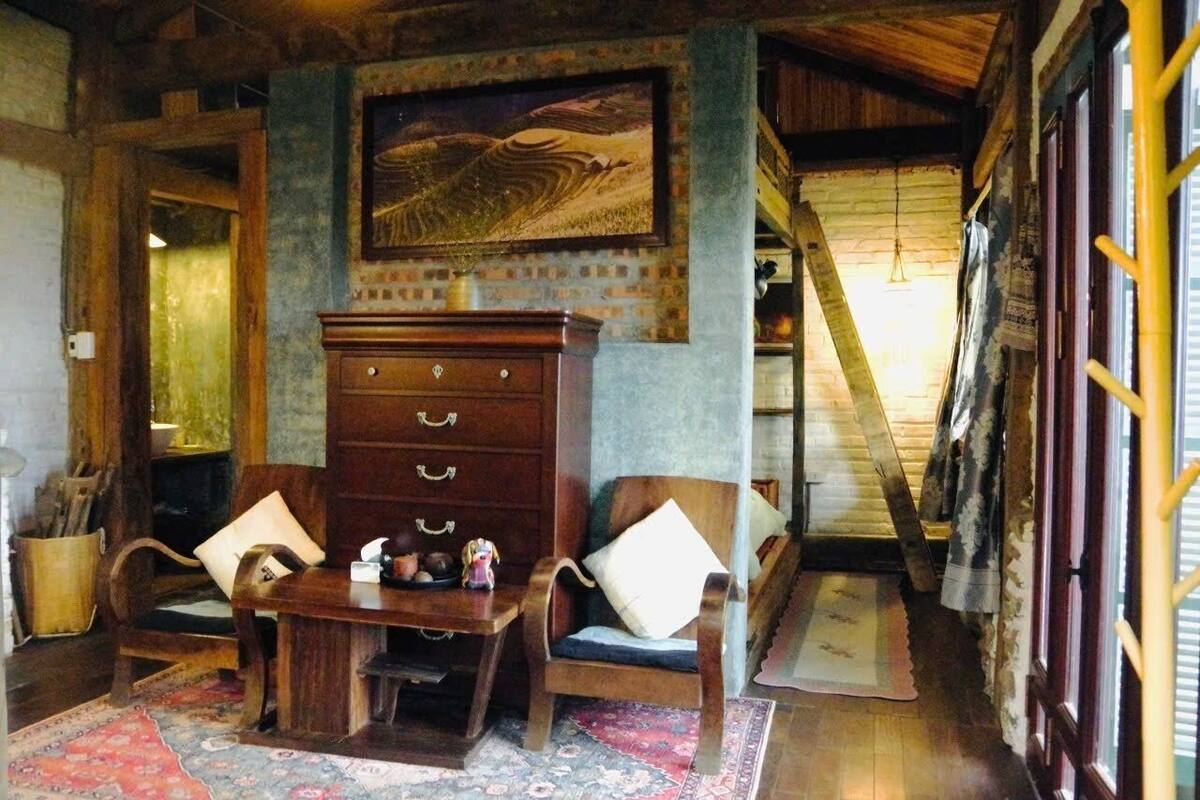 Um quarto acolhedor com cômoda de madeira, duas cadeiras, tapete e um quadro na parede.