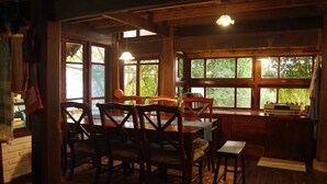 Un coin repas en bois avec une table et des chaises, de grandes fenêtres donnant sur un paysage verdoyant et un intérieur rustique.