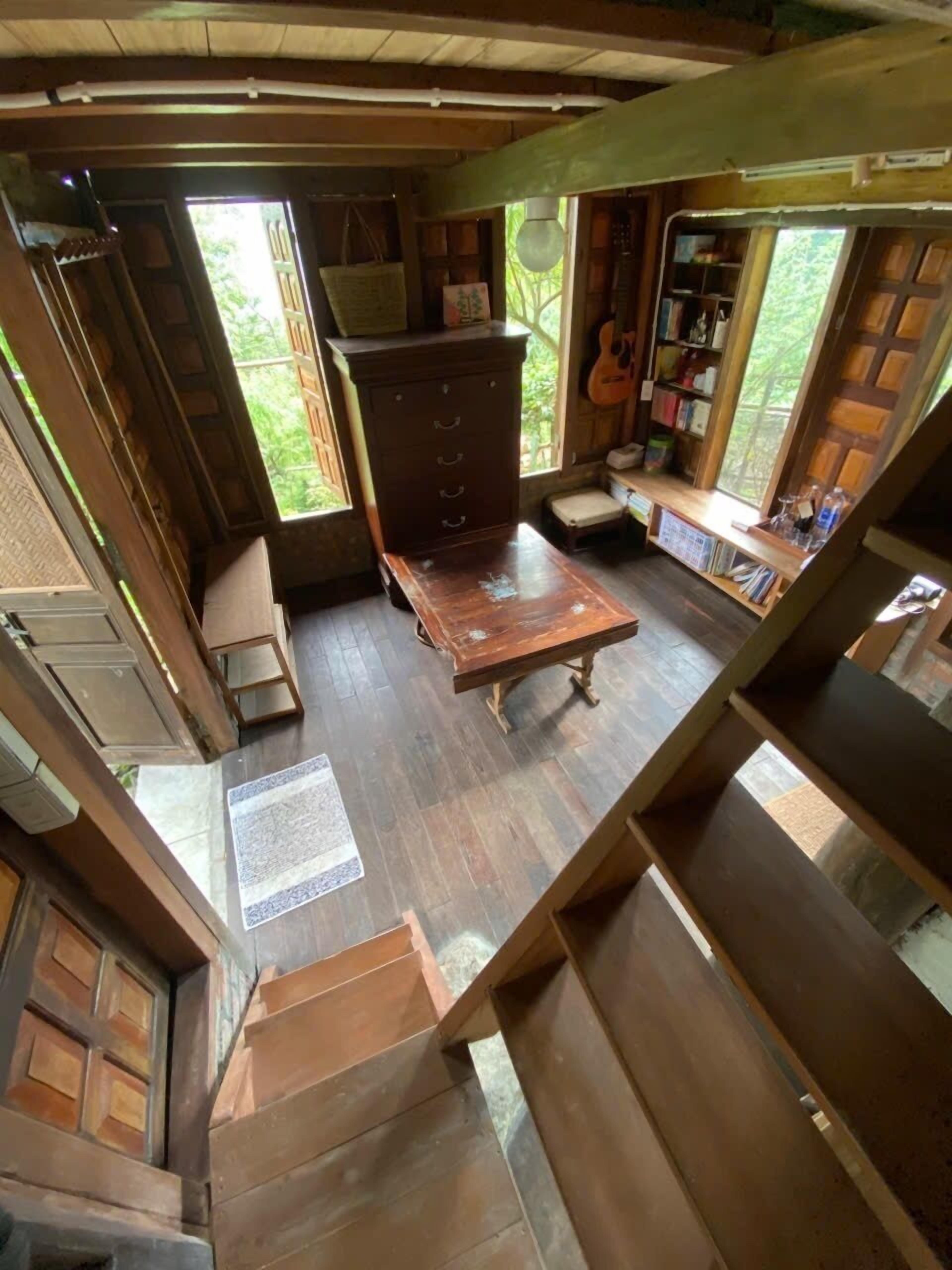 A loft-style room with a wooden floor, a central table, a bench, and a bookshelf.