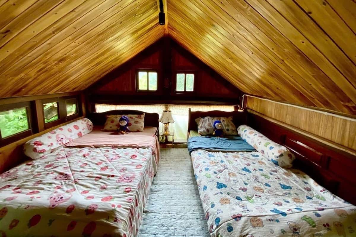 Um quarto de sótão acolhedor com duas camas, ripas de madeira no teto e janelas nas paredes.