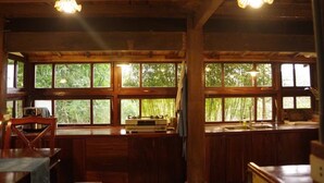 Un intérieur rustique en bois, avec de grandes fenêtres, des poutres apparentes et un coin repas comprenant une table et des chaises.
