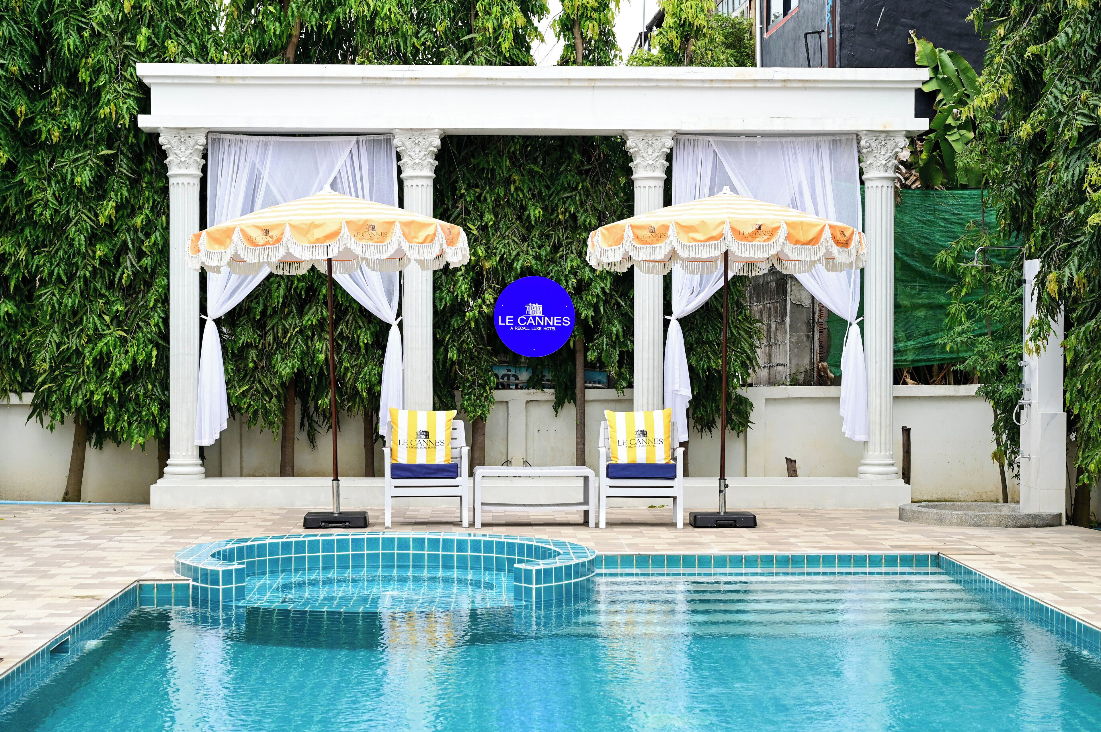 A pool area with two lounge chairs, a canopy, and a sign for Le Cannes A Recall Luxe Hotel.