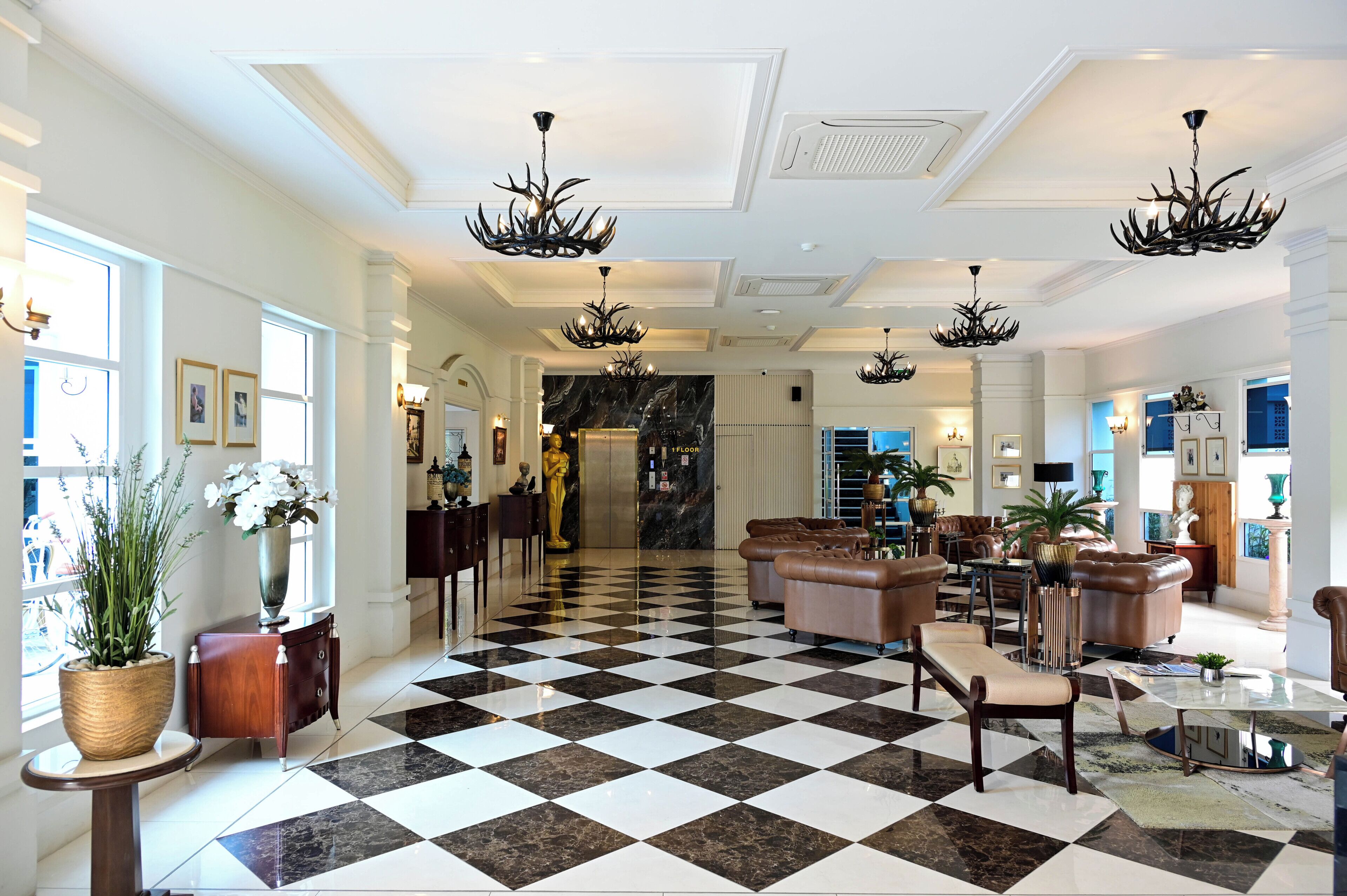A hotel lobby with a checkered floor, leather sofas, chandeliers, and a marble wall.