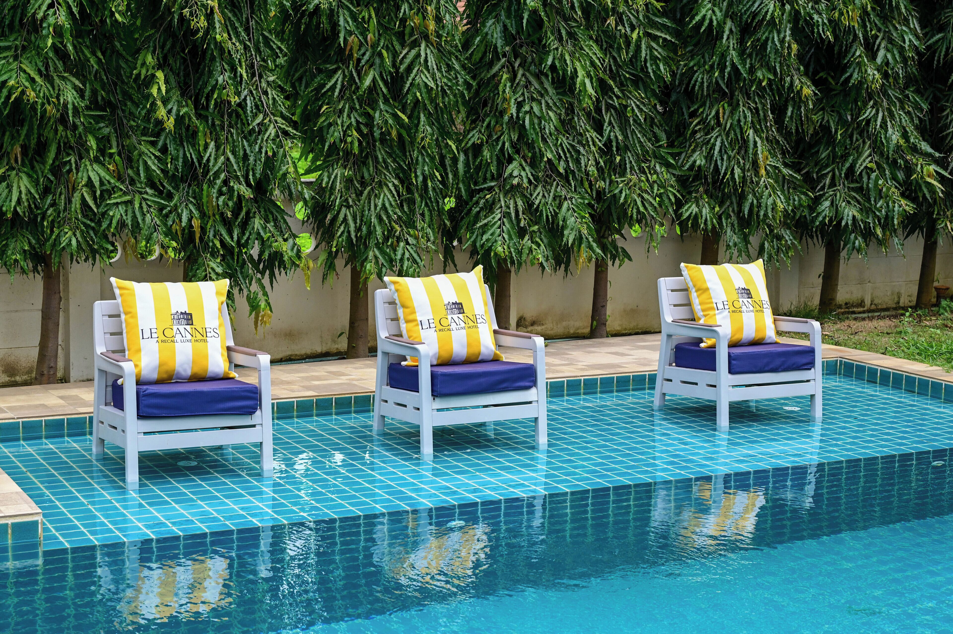 Zona de piscina amb tres gandules, cada una amb coixí i almoadí que mostren el logotip de l'hotel.