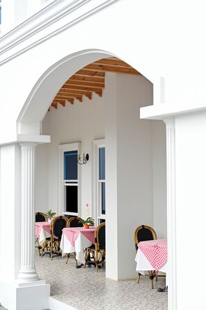 A covered outdoor seating area with tables and chairs, a wooden ceiling, and a white building facade. - Le Cannes Hotel  (Chiang Mai)