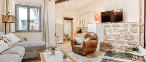 A spacious living area with a sofa, armchair, and a dining table. A stone fireplace and a television are also visible.