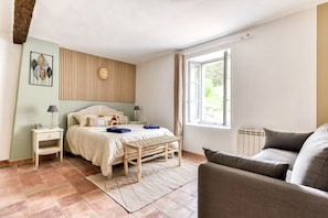 Ein Schlafzimmer mit Bett, Nachttisch, Lampe, Bank und einem Fenster mit Vorhängen.