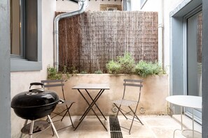 Eine Terrasse mit Grill, zwei Stühlen und einem Tisch.